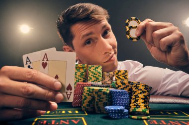 Beyaz gömlekli iyi görünümlü bir adamın yakın plan çekimi, kumarhanenin masasında beyaz bir spot ışığına karşı duman içinde poker oynamaktır. Elindeki iki ası ve çipi göstererek zaferine seviniyor. Kumar bağımlılığı. Samimi duygular ve giriş
