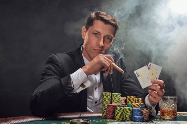 Siyah takım elbiseli ve beyaz gömlekli şık bir adam kumarhanedeki masada beyaz bir spot ışığına karşı duman içinde poker oynuyor. Elindeki iki ası göstererek, puro içerek ve kameraya bakarak kazandığı zafere seviniyor. Kumar bağımlısı.