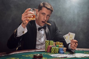 Siyah ve beyaz gömlekli şık bir erkek kumarhanede beyaz spot ışıklarına karşı duman içinde poker oynuyor. Puro içerken, alkol içerken ve iki as gösterirken zaferine seviniyor. Kumar bağımlılığı. O zamandan