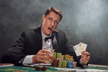 Siyah takım elbiseli ve beyaz gömlekli şık bir adam kumarhanede beyaz spot ışıklarına karşı duman içinde poker oynuyor. Puro içerken, alkol içerken ve iki as gösterirken zaferine seviniyor. Kumar bağımlılığı. Samimi ol.