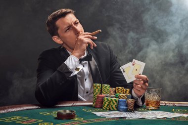 Siyah takım elbiseli ve beyaz gömlekli şık bir adam kumarhanedeki masada beyaz bir spot ışığına karşı duman içinde poker oynuyor. Elindeki iki ası göstererek ve puro içerek zaferine seviniyor. Kumar bağımlılığı. Samimi duygular
