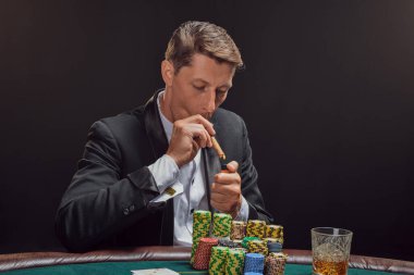 Siyah ve beyaz gömlekli kibirli bir erkek kumarhanede beyaz bir spot ışığına karşı duman içinde poker oynuyor. Puro içerek zaferine seviniyor. Kumar bağımlılığı. Samimi duygular ve eğlence konsepti.