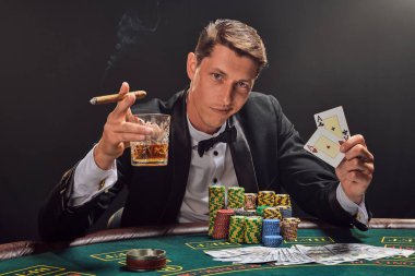 Siyah takım elbiseli ve beyaz gömlekli yakışıklı kumarhanenin masasında beyaz spot ışıklarına karşı duman içinde poker oynuyor. Elinde iki as, elinde bir bardak viski, puro ve göz kırparak zaferini kutluyor.