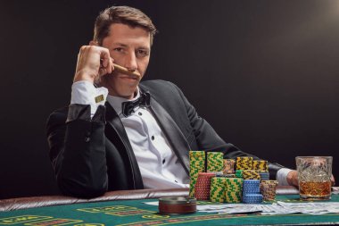 Siyah takım elbiseli ve beyaz gömlekli kibirli bir adam kumarhanenin masasında beyaz bir spot ışığına karşı duman içinde poker oynuyor. Bir puro kokluyor ve sana bakıyor. Kumar bağımlılığı. Samimi duygular ve eğlence konsepti.
