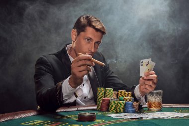 Siyah ve beyaz gömlekli zeki bir erkek kumarhanedeki masada beyaz bir spot ışığına karşı duman içinde poker oynuyor. Elindeki iki ası göstererek zaferine seviniyor, puro içiyor ve başka tarafa bakıyor. Kumar bağımlılığı. O zamandan