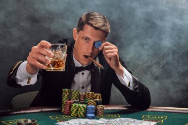 Siyah ve beyaz gömlekli şık bir insan, beyaz bir spot ışıklarına karşı kumarhanede duman içinde poker oynuyor. Viski içerek, puro içerek, cips yiyerek ve kameraya bakarak zaferini kutluyor.