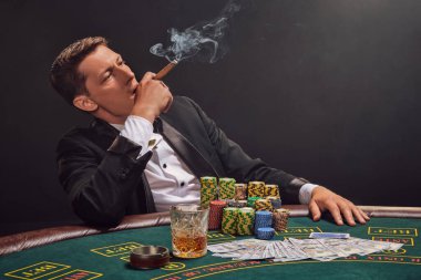 Siyah ve beyaz tişörtlü görkemli kişi kumarhanedeki masada beyaz bir spot ışığına karşı duman içinde poker oynuyor. O bir puro içiyor ve yukarı bakıyor. Kumar bağımlılığı. Samimi duygular ve eğlence konsepti.