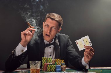 Siyah ve beyaz gömlekli yakışıklı bir adam kumarhanedeki masada beyaz bir spot ışığına karşı duman içinde poker oynuyor. Elindeki iki ası göstererek, puro içerek ve kameraya bakarak kazandığı zafere seviniyor. Kumar katkı maddesi