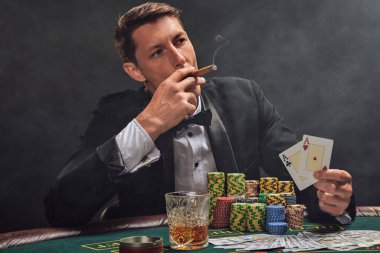 Siyah takım elbiseli ve beyaz gömlekli şık bir adam kumarhanenin masasında beyaz bir spot ışığına karşı duman içinde poker oynuyor. Elindeki iki ası göstererek, puro içerek ve yüzünü çevirerek zaferine seviniyor. Kumar bağımlılığı. Samimi. 