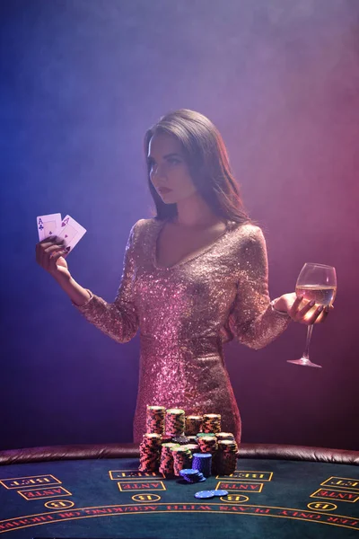 Chica morena con un peinado perfecto y maquillaje brillante está posando con cartas y una copa de champán en sus manos. Casino, poker . —  Fotos de Stock