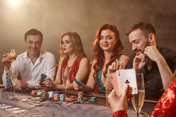 快乐的朋友们在赌场打扑克 在黑暗的烟幕下 年轻人在白光的映衬下 坐在桌边 等待着大胜 娱乐概念 — 图库照片