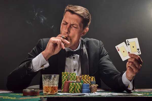 Siyah ve beyaz gömlekli yakışıklı bir adam kumarhanedeki masada beyaz bir spot ışığına karşı duman içinde poker oynuyor. Elindeki iki ası göstererek ve puro içerek zaferine seviniyor. Kumar bağımlılığı. Samimi emoti.