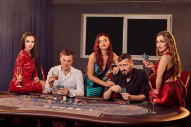 Bir grup genç gülen arkadaş kumarhanede poker masasında oynuyorlar ve mutlu görünüyorlar. Gençler büyük bir galibiyet için bahis oynuyorlar. Para için kumar oynuyorum. Şans oyunları..