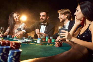 Üst sınıf arkadaşlar kumarhanede kumar oynuyorlar. Takım elbiseli iki adam ve elbiseli iki genç kadın. Tüttür. Kumarhane. Poker