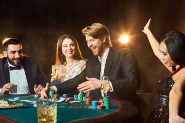 Üst sınıf arkadaşlar kumarhanede kumar oynuyorlar. Takım elbiseli iki adam ve elbiseli iki genç kadın. Tüttür. Kumarhane. Poker