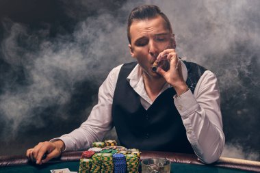 Beyaz gömlekli ve siyah yelekli ciddi bir olgun adam masada oturmuş puro içiyor. Bir kumarhanede, arka plandaki siyah dumanlı bir ışıkta, heyecanla poker oynuyor. Kartlar ve fişler ile riskli kumar eğlencesi.