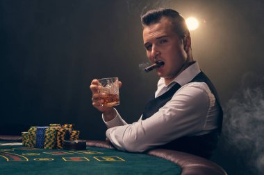 Beyaz gömlekli ve siyah yelekli yakışıklı bir adam puro içiyor ve elinde bir bardak viski tutuyor. Kumarhanede siyah arka planda bir ışık hüzmesiyle poker oynuyor. Ka ile riskli kumar eğlencesi