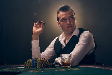 Beyaz gömlekli ve siyah yelekli zengin bir adam elinde bir puro tutuyor ve başka tarafa bakıyor. Kumarhanede arka planda siyah arka planda poker oynuyor. Kartlar ve fişler ile riskli kumar eğlencesi.