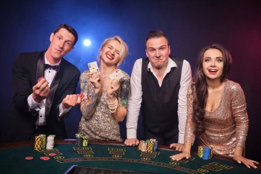 Mutlu ve zengin bir grup kumarhanede poker oynuyor. Gençler büyük bir galibiyet için bahis oynuyorlar. Masada, siyah arka planda kırmızı ve mavi bir arka ışığa karşı gülümsüyorlar. Riskli kumar eğlencesi.