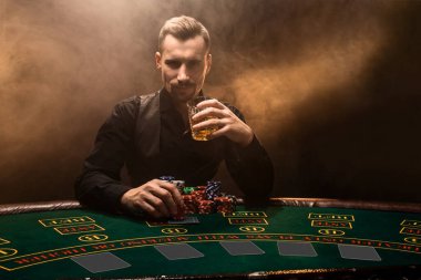 Poker masasında oturan takım elbiseli genç bir adam. Adam kumar oynar. Oyun masasındaki iskambil oynayan oyuncu. Poker. Kumarhane
