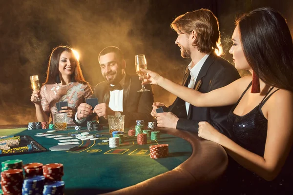 Upper class friends gambling in a casino. Two men in suits and two young women in dresses. Smoke. Casino. Poker