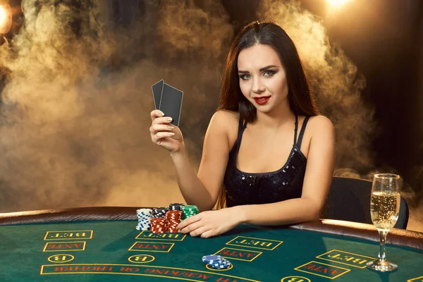 シャンパンのガラスとポーカーテーブルに座って黒のドレスでゴージャスな感情的な若い女性 煙を出して ポーカーだ カジノ — ストック写真