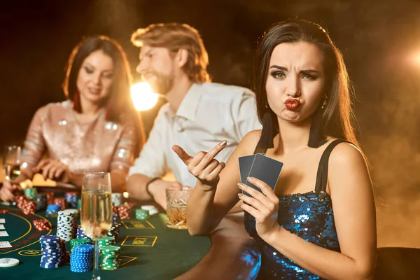 一群优雅的人在赌场打扑克 专注于穿着蓝色闪亮连衣裙的情绪化的黑发女人 它是一种娱乐 为了钱玩危险的卡牌游戏 烟熏背景 — 图库照片