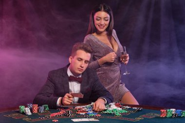 Kumarhanede poker oynayan bir adam masasında yığınla fiş, para, şampanya ve kartlarla oturuyor. Kadınlarla kazanmayı kutluyoruz. Siyah arka plan. Yakın plan..