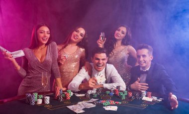 Kumarhanede poker oynayan arkadaşlar. Zaferlerini kutluyorlar, şampanya içiyorlar ve masada üzerinde bir yığın fiş, para ve kartla poz veriyorlar..