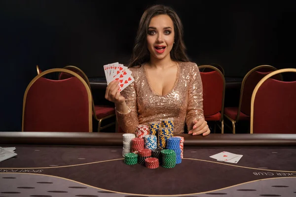 Mulher morena bonita está jogando poker sentado à mesa no cassino . — Fotografia de Stock