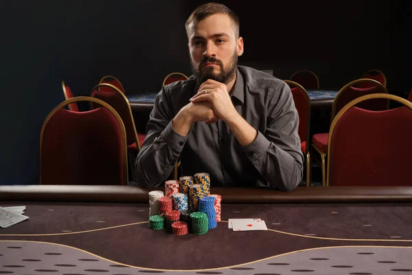 Красивий бородатий чоловік грає в покер, сидячи за столом в казино . — стокове фото