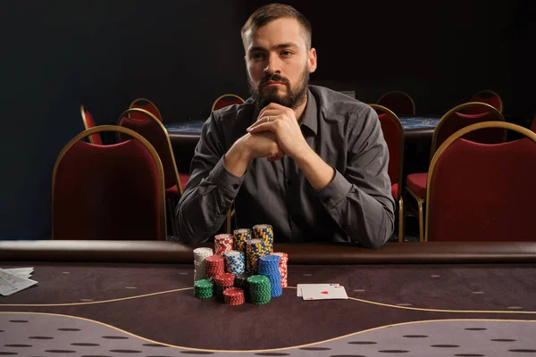 Hombre barbudo guapo está jugando póquer sentado en la mesa en el casino . — Foto de Stock