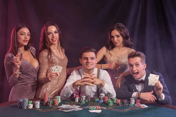 友人は カジノでポーカーをプレイ チップのスタックとテーブルで それにカード 勝利を楽しむシャンパンを飲み 煙の背景 カラフルなバックライト ギャンブルだ — ストック写真