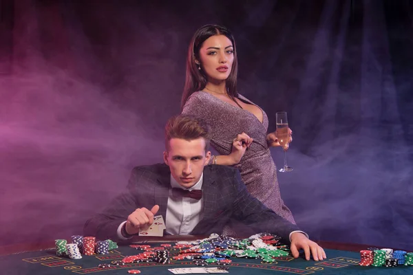 Kumarhanede poker oynayan bir adam masasında yığınla fiş, para, şampanya ve kartlarla oturuyor. Kadınlarla kazanmayı kutluyoruz. Siyah arka plan. Yakın plan.. — Stok fotoğraf