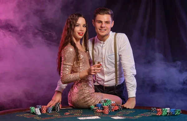 Hombre y mujer jugando al póquer en el casino, celebrando la victoria en la mesa con montones de fichas, cartas, champán. Negro, fondo de humo. Primer plano . — Foto de Stock