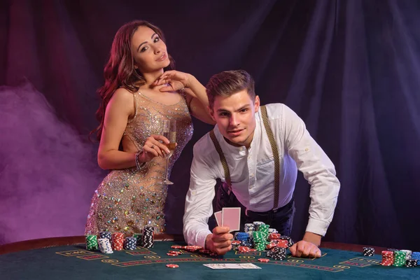 Man and woman playing poker at casino, celebrating win at table with stacks of chips, cards, champagne. Black, smoke background. Close-up. — Stock Photo, Image