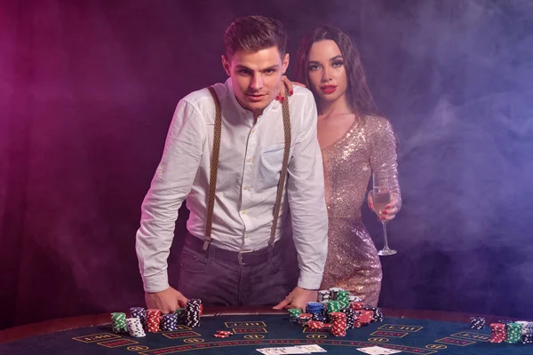 Kumarhanede poker oynayan erkek ve kadın, masada bir yığın fiş, kart ve şampanyayla kazanmayı kutluyorlar. Siyah, dumanlı arka plan. Yakın plan.. — Stok fotoğraf