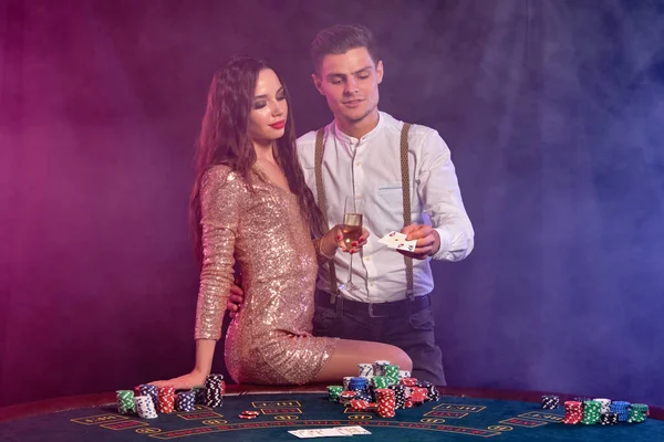 Άντρας και γυναίκα παίζουν πόκερ στο καζίνο, γιορτάζοντας τη νίκη στο τραπέζι με στοίβες από μάρκες, κάρτες, σαμπάνια. Μαύρο, φόντο καπνού. Κοντινό πλάνο. — Φωτογραφία Αρχείου