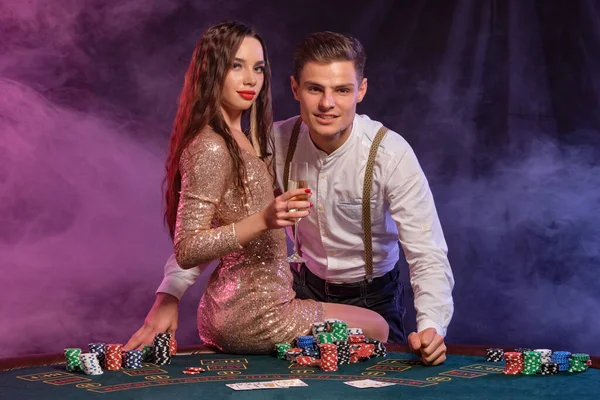 Homme et femme jouant au poker au casino, célébrant la victoire à table avec des piles de jetons, cartes, champagne. Noir, fond de fumée. Gros plan . — Photo