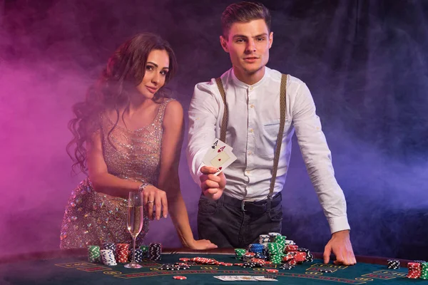 Hombre y mujer jugando al póquer en el casino, celebrando la victoria en la mesa con montones de fichas, cartas, champán. Negro, fondo de humo. Primer plano . — Foto de Stock