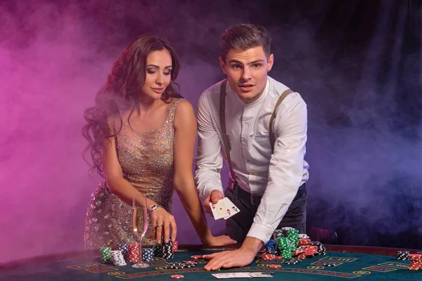 カジノでポーカーをプレイする男と女,チップのスタックでテーブルで勝利を祝う,カード,シャンパン.黒煙の背景だ。閉鎖. — ストック写真