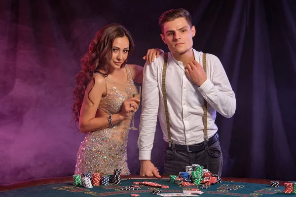 Hombre y mujer jugando al póquer en el casino, celebrando la victoria en la mesa con montones de fichas, cartas, champán. Negro, fondo de humo. Primer plano . — Foto de Stock