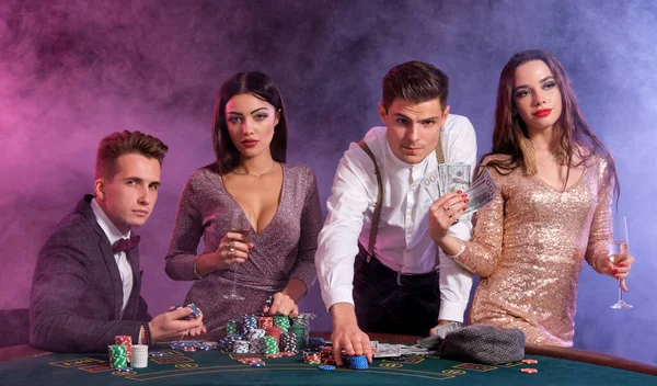 Amici che giocano a poker al casinò. Festeggiano la loro vittoria, bevono champagne e posano al tavolo con pile di patatine, soldi e carte sopra. . — Foto Stock