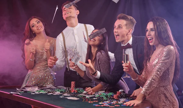 Friends playing poker at casino, at table with stacks of chips, money, cards, champagne on it. Celebrating win, excited. Black background. Close-up. — ストック写真