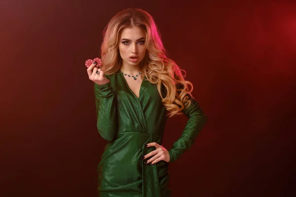 Ξανθιά σγουρή γυναίκα με φωτεινό μακιγιάζ, σε πράσινο στυλάτο φόρεμα και κοσμήματα. Εμφάνιση δύο κόκκινες μάρκες, ποζάρουν σε πολύχρωμο καπνιστό φόντο. Κοντινό πλάνο — Φωτογραφία Αρχείου