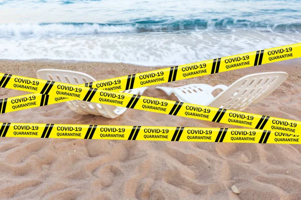 Biohazard Coronavirus warning tapes against two empty white deck chairs on sandy beach with view on blue sea, Egypt. Quarantine. Worldwide pandemic COVID-19, 2019-nCoV, SARS-CoV-2. Infectious disease