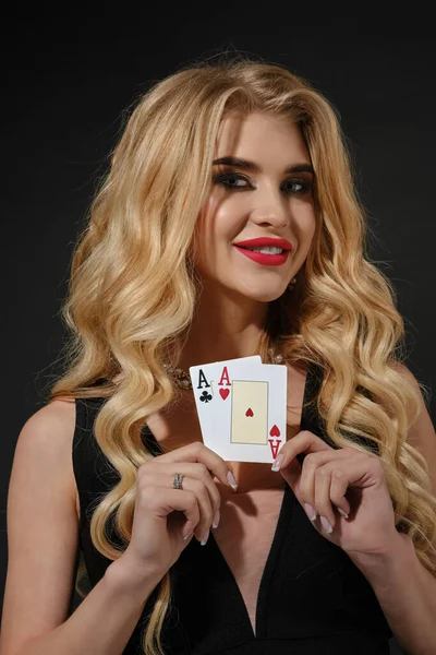 Modelo rubio en negro elegante vestido y collar. Ella sonrió, mostrando dos ases, posando sobre fondo negro. Poker, casino. Primer plano —  Fotos de Stock