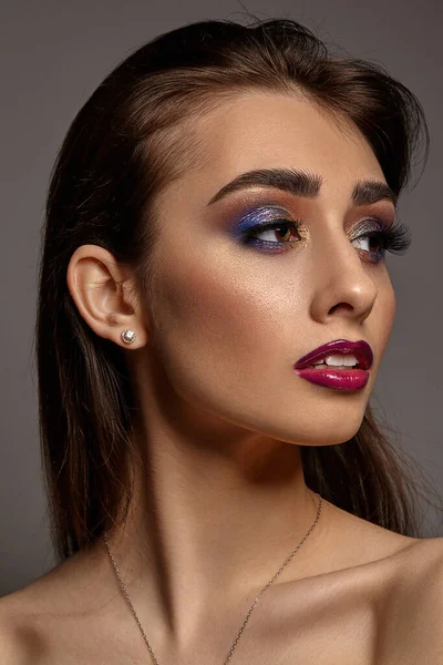 Brünette nackte Frau in Schmuck posiert auf grauem Studiohintergrund. Luxus-Make-up. Bunter Lidschatten, lange Wimpern, glänzend rote Lippen. Nahaufnahme — Stockfoto