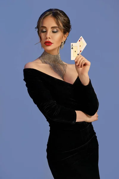Mujer morena con hombros desnudos, en vestido negro y joyas. Mostrando dos cartas, posando sobre fondo azul. Poker, casino. Primer plano — Foto de Stock