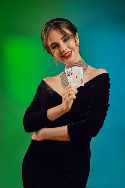 ブラックドレス、光沢のあるネックレスとイヤリングのブルネットの女性。彼女は笑顔で、 2つの顔を見せ、カラフルな背景にポーズをとっています。ポーカー、カジノ。閉鎖 — ストック写真